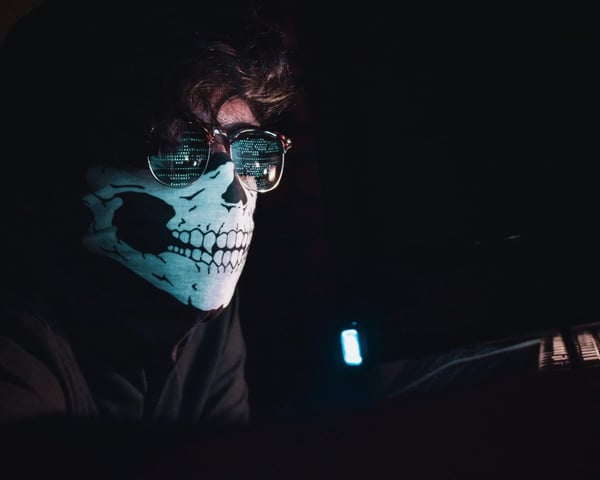 A person wearing a skeleton mask and sunglasses in a dark room.