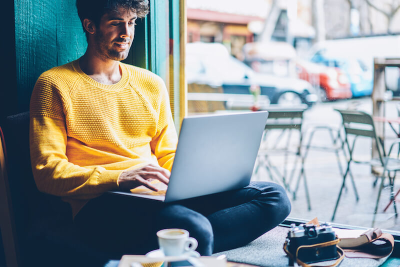 Man in a yellow shirt sitting in the window of a cafe using a laptop.