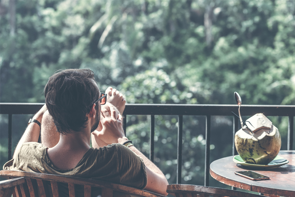 shot of man relaxing on balcony drinking from coconut