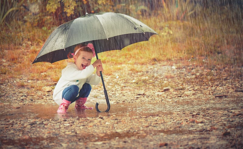 small girl smiling under umbrella in the rain