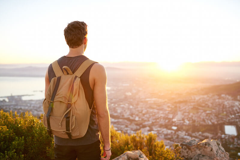 man standing on hill gazing at sunset