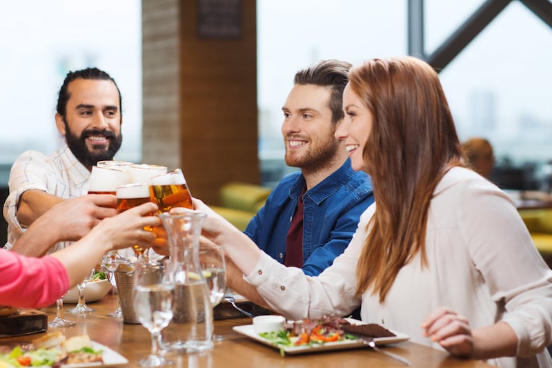 friends sitting at table cheering with beer glasses