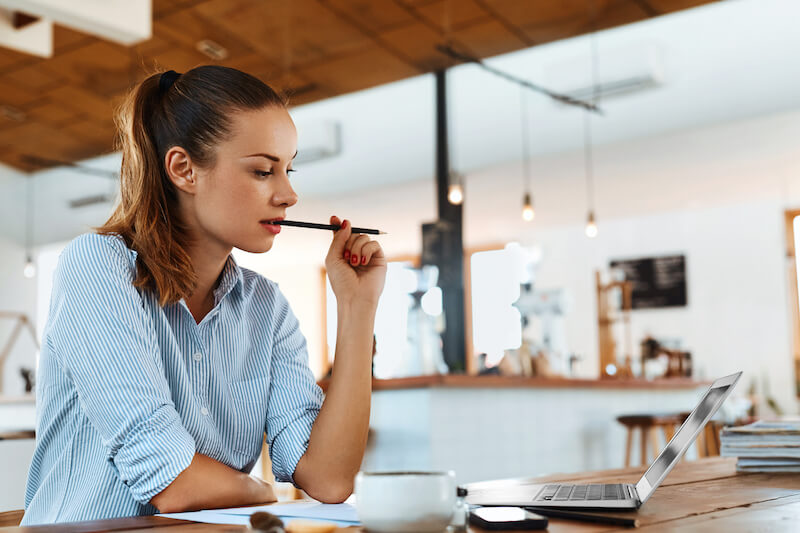 woman wearing glasses working at laptop with pencil