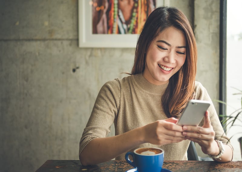 woman smiling using mobile phone at table in cafe