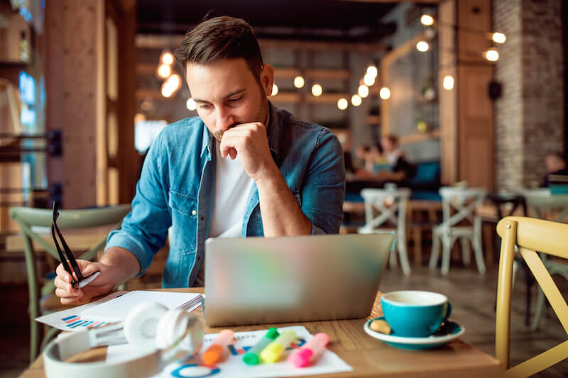 worried man wearing glasses sitting at table with laptop and paper